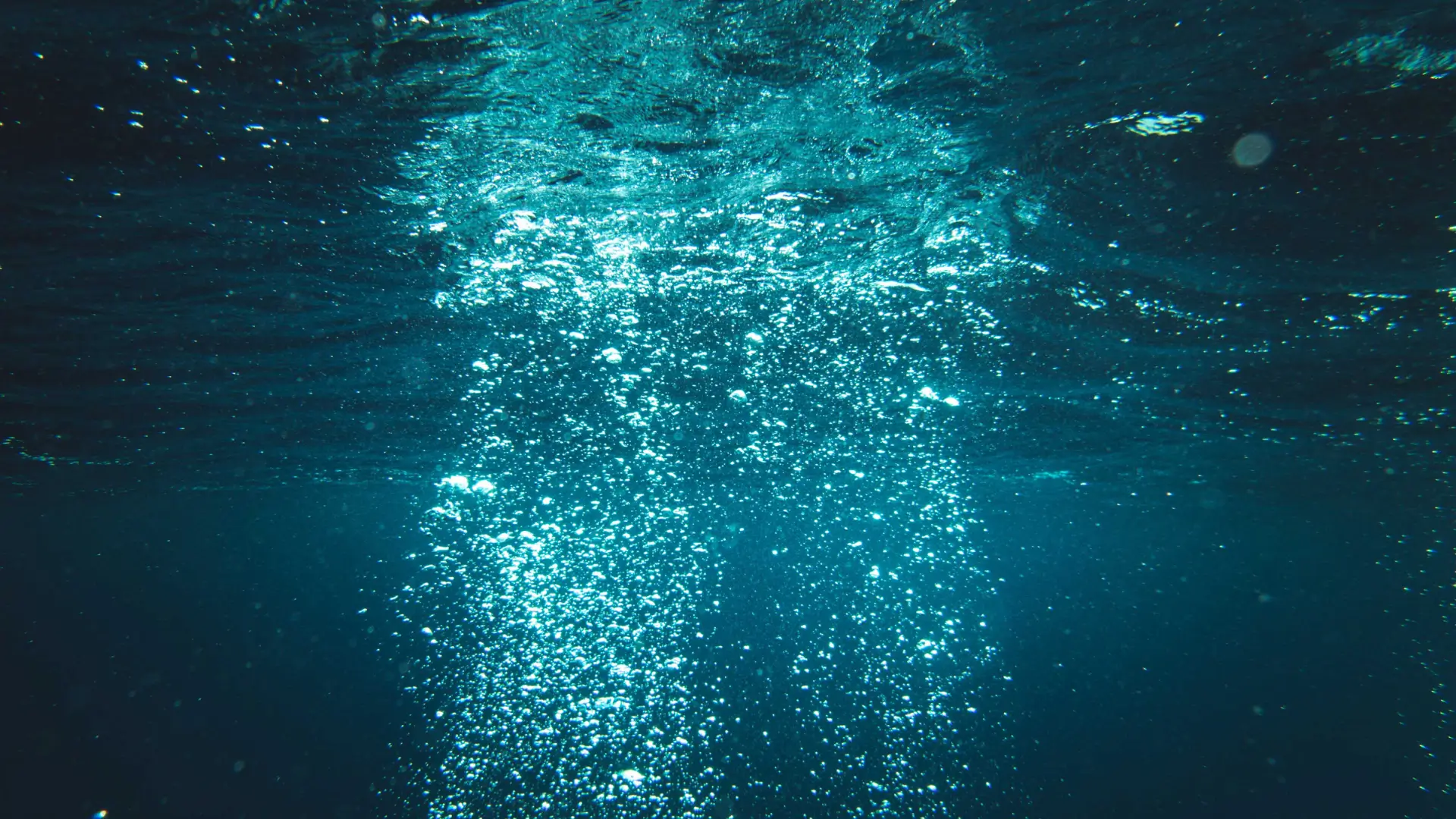 Colonne de bulles d'air remontant vers la surface éclairée d'une eau bleu profond